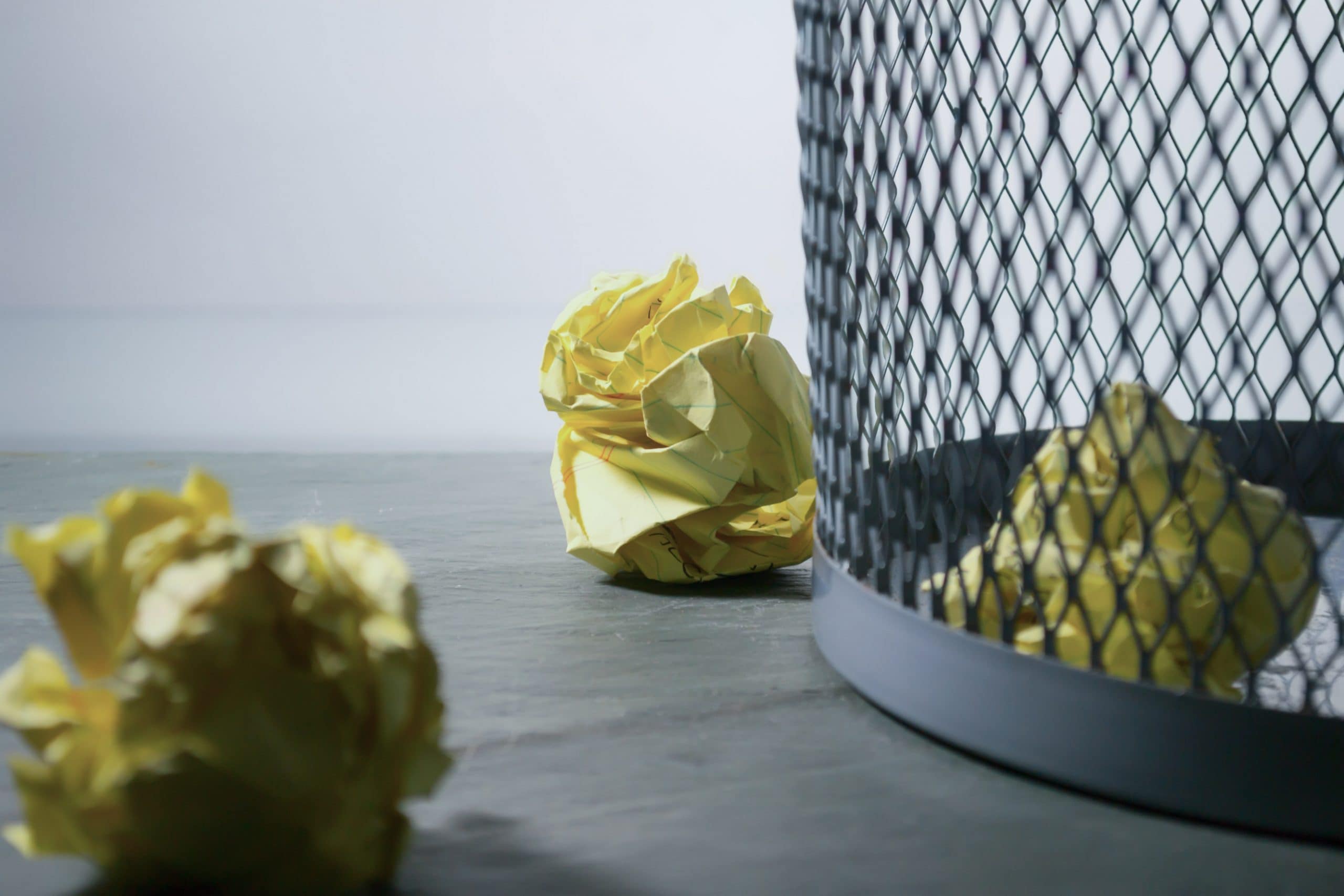 Bin with several pieces of scrunched up yellow paper in it and near it