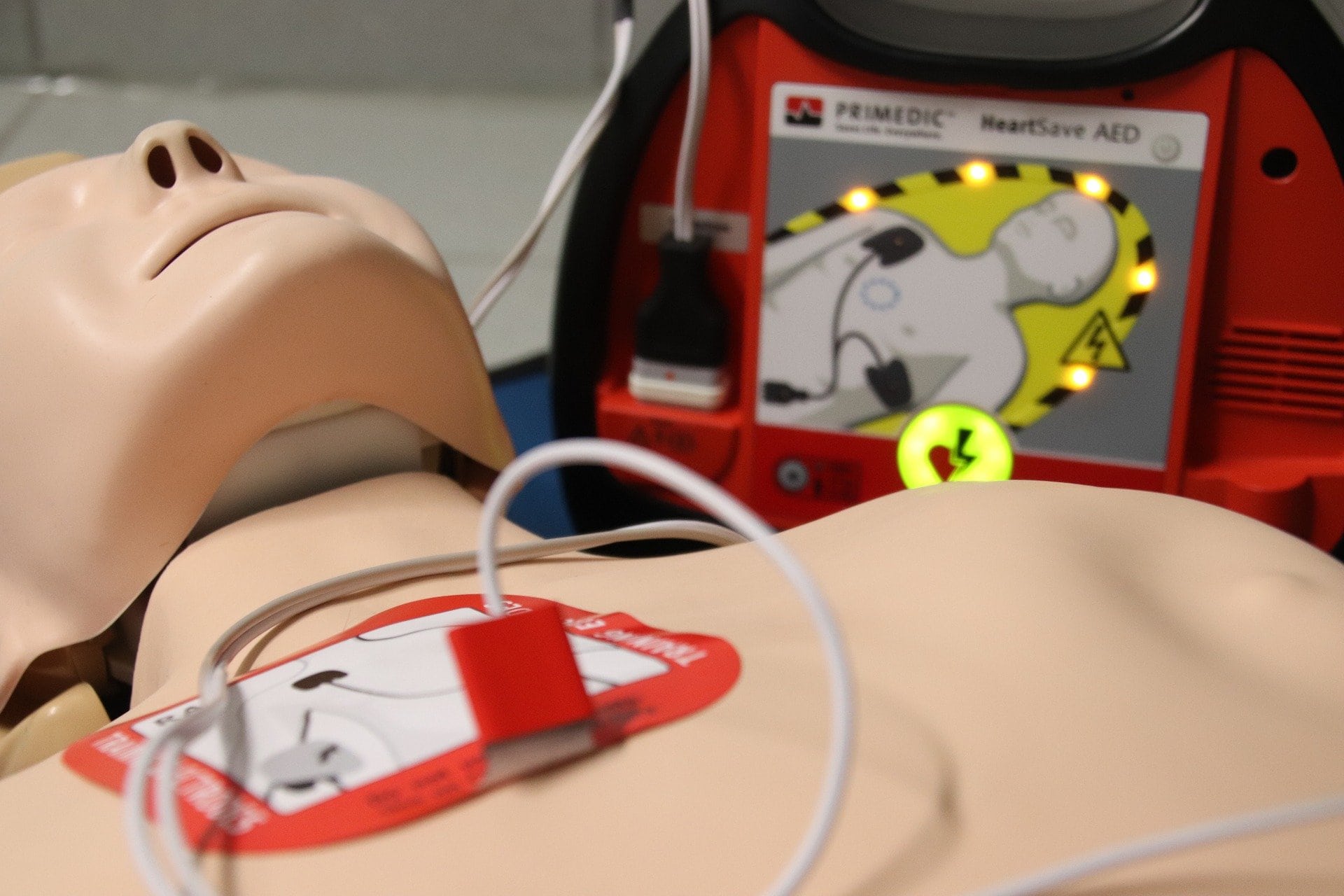 Resuscitation dummy next to a defibrillator - one of the defibrillator pads is on the dummy's chest.