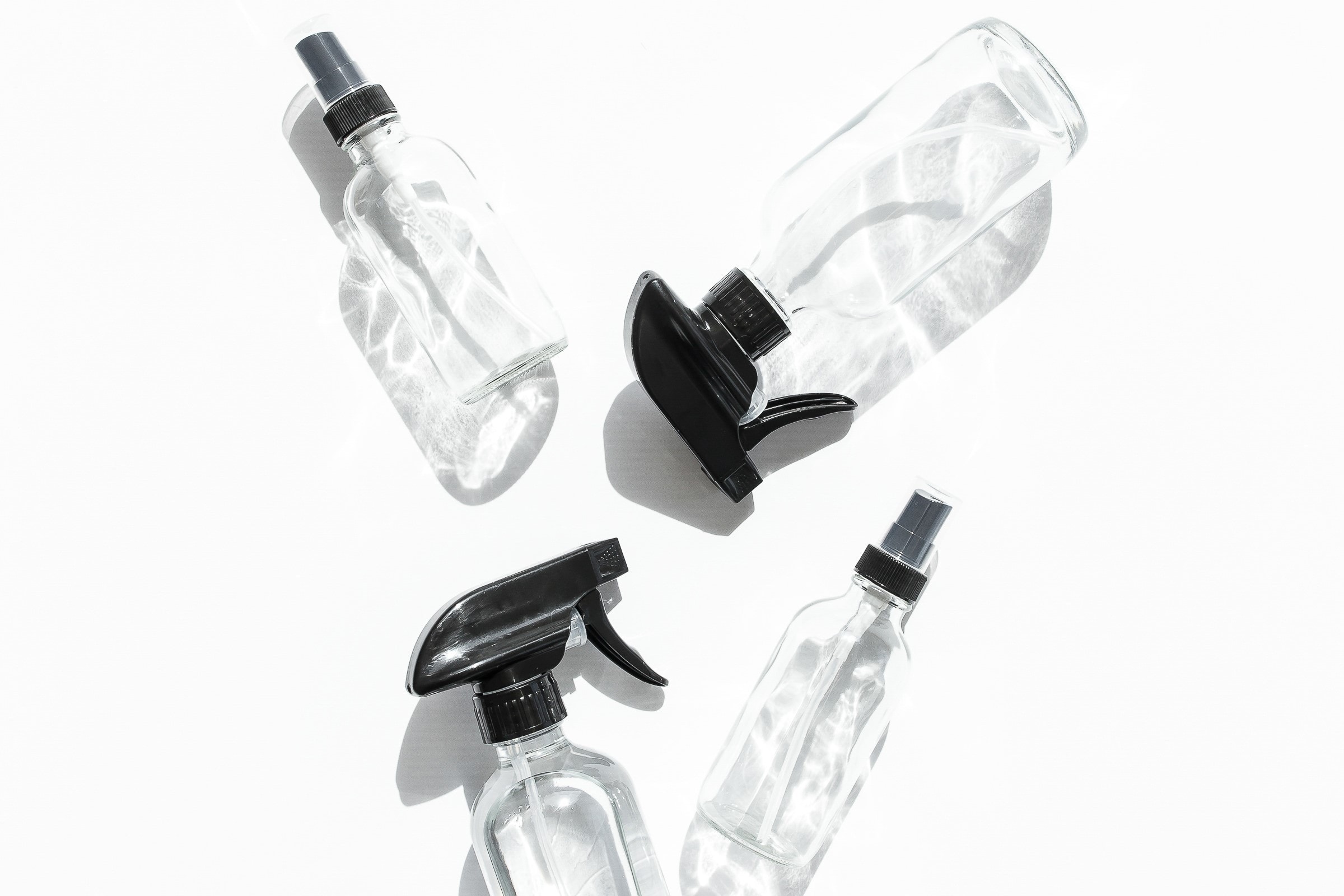 4 clear spray bottles on a white background. They are the sort of bottles you might use for cleaning products.