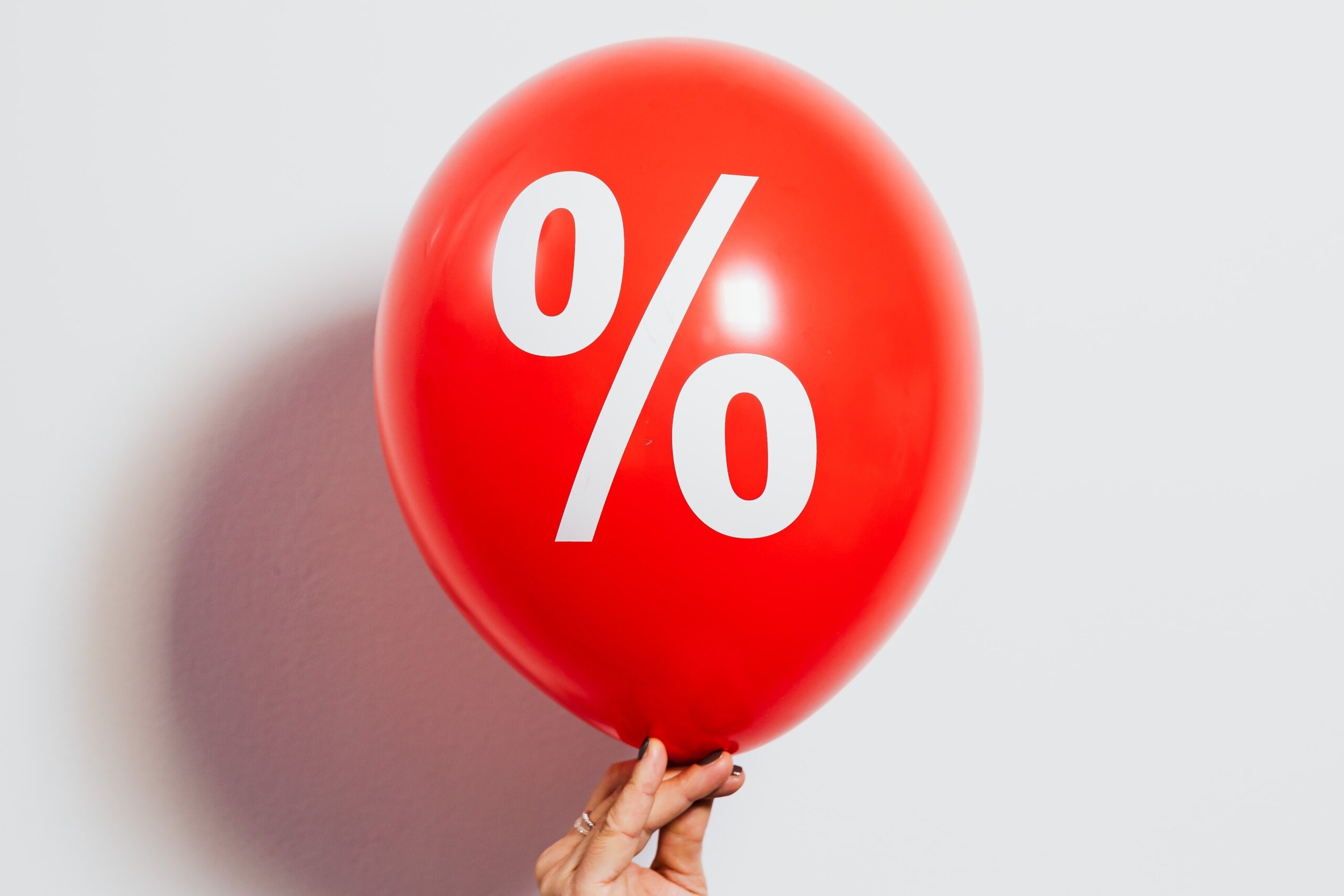 Woman's hand holding up a red balloon with a % symbol written on it