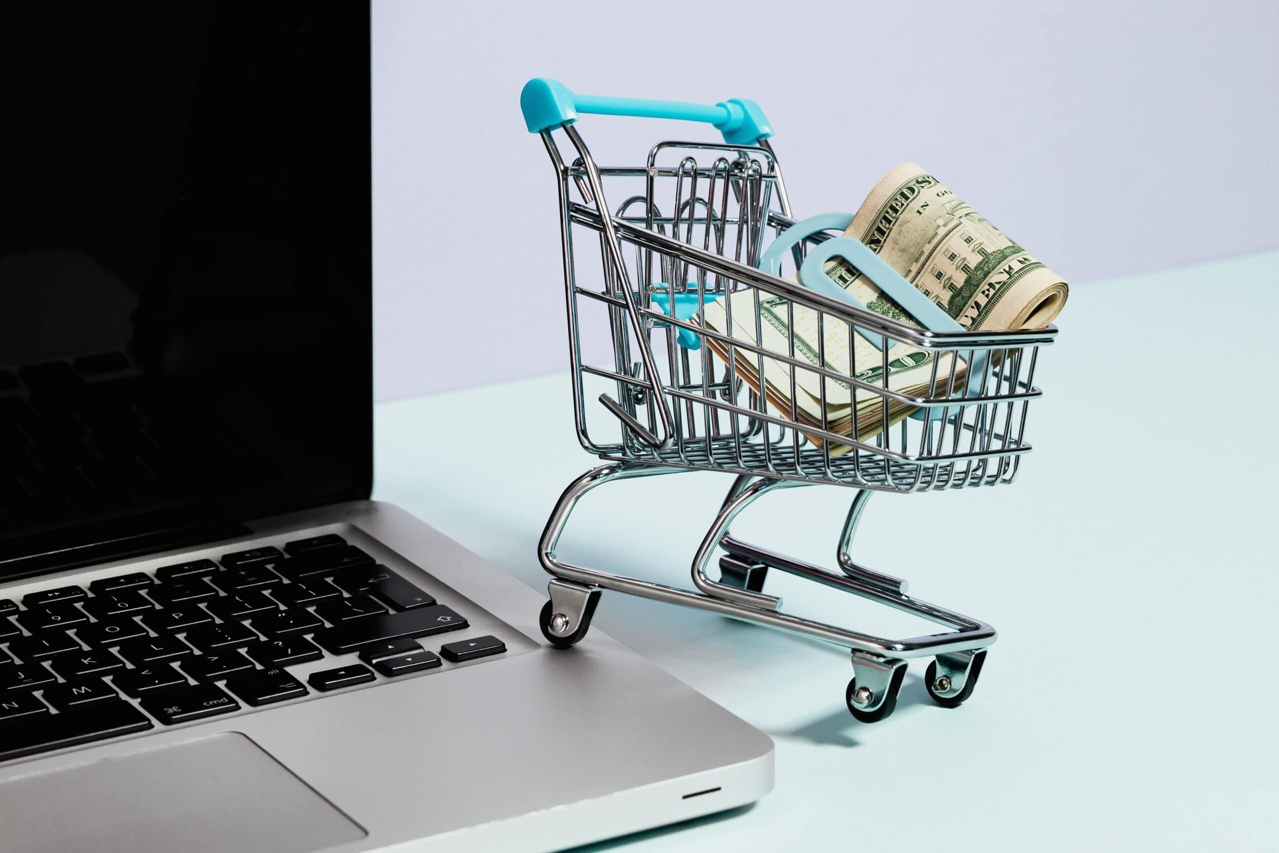 Tiny shopping cart filled with banknotes next to a laptop